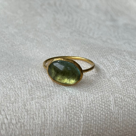 22ctGold ring with a green tourmaline gemstone on a textured beige surface