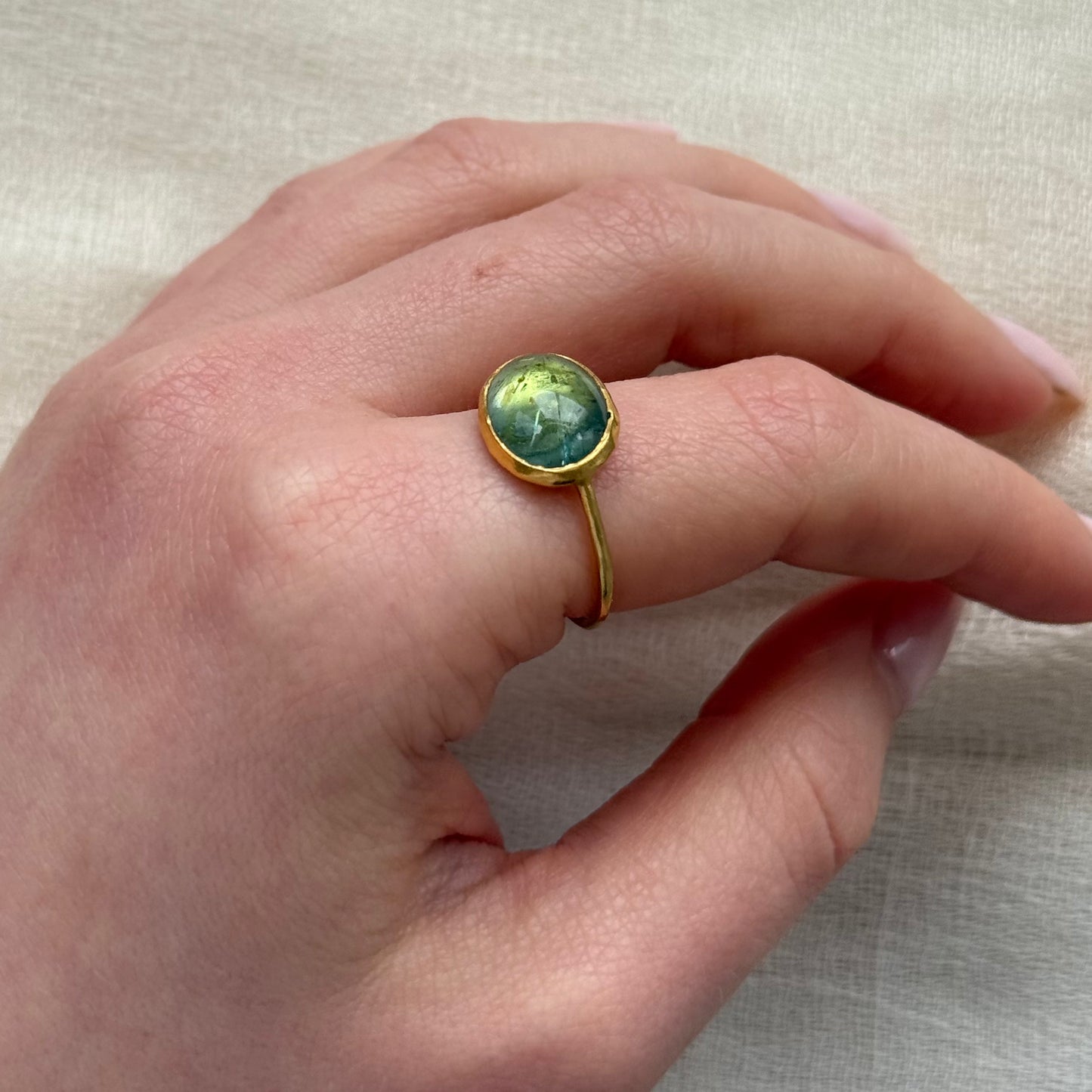 Hand wearing a 22ct gold ring with a green tourmaline gemstone on a neutral background