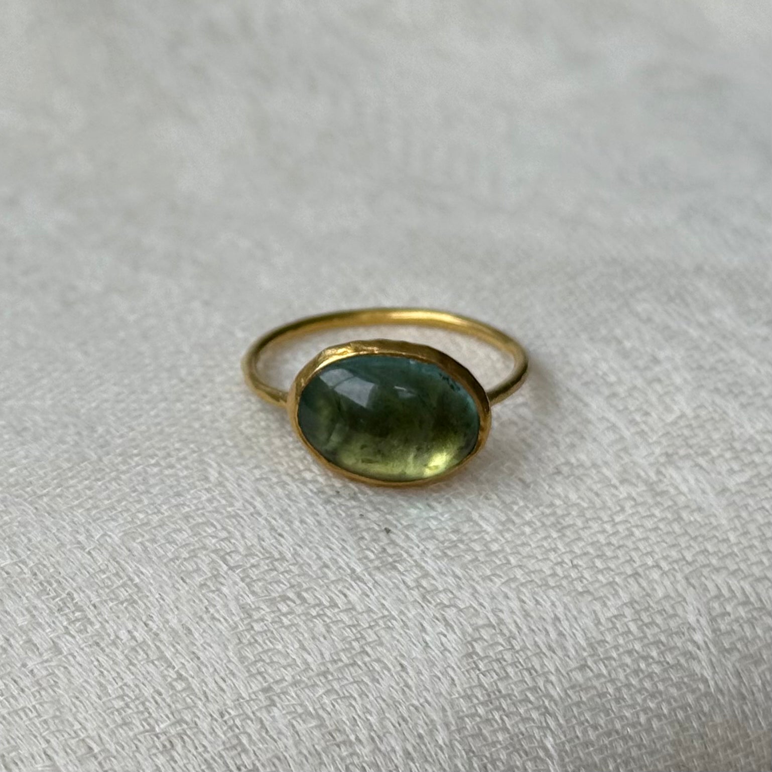 22ct Gold ring with a green tourmaline gemstone on a light gray fabric background