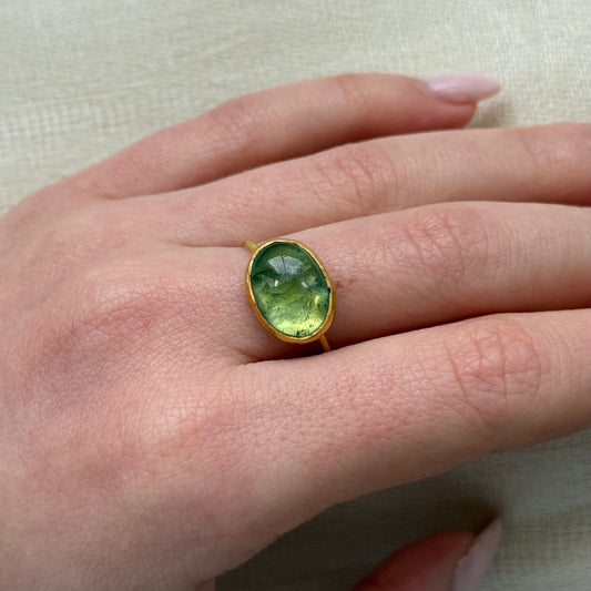 Hand wearing a green tourmaline gemstone ring with 22ct gold band on a light background