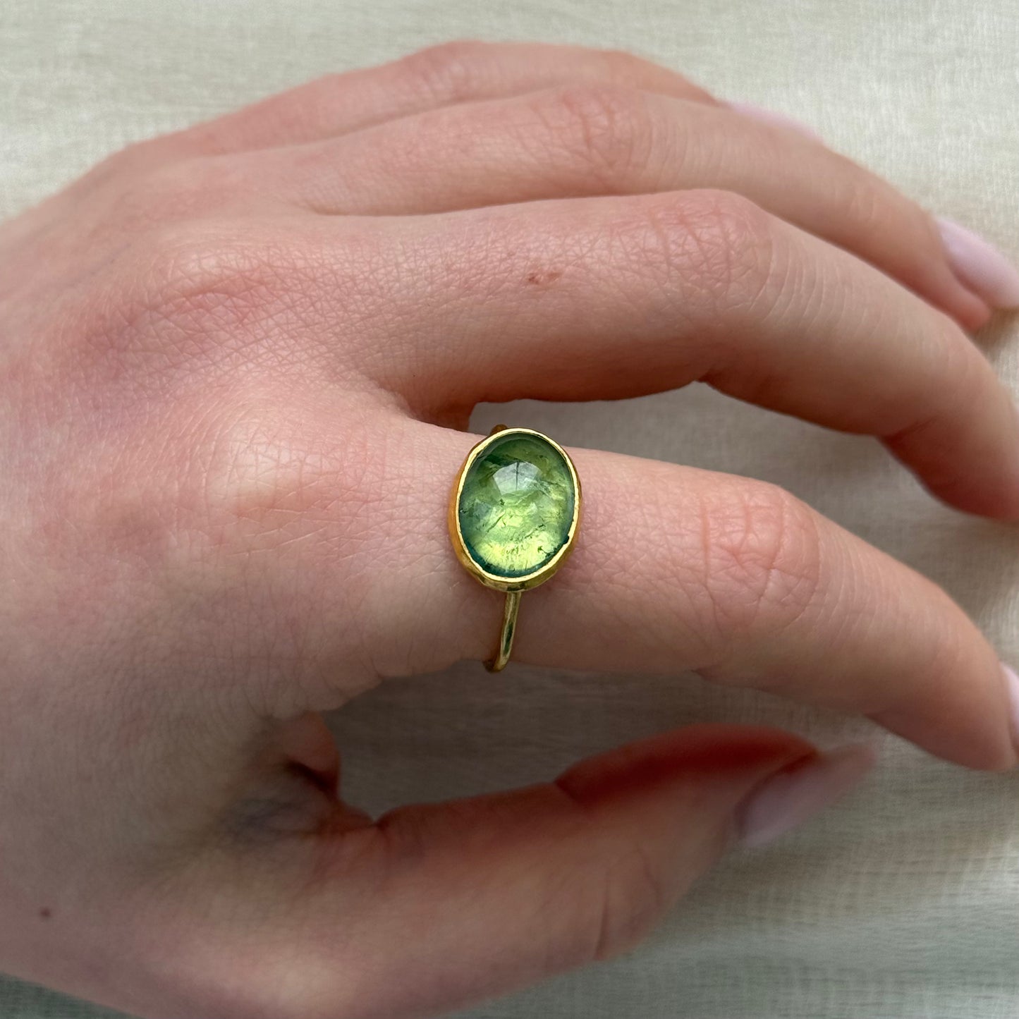 Hand wearing a 22ct gold ring with a green tourmaline gemstone on a neutral background