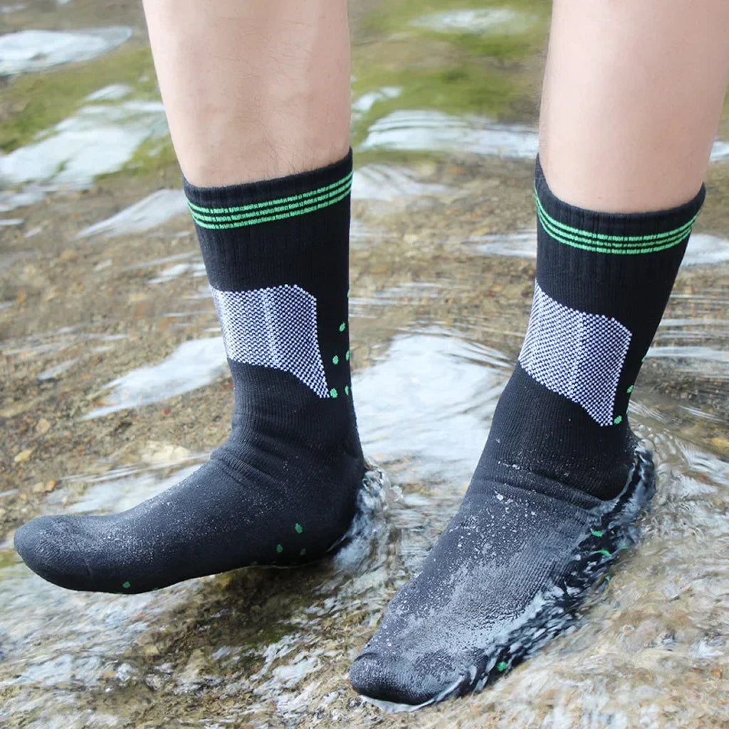 Person wearing black socks with green stripes and gray water shoes standing in water.