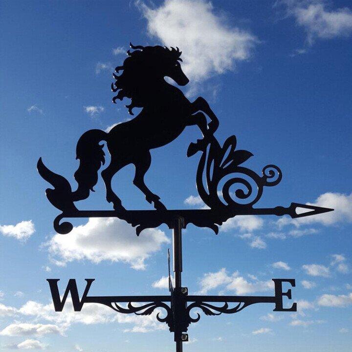 Silhouette of a rearing horse weather vane against a blue sky with clouds