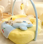 Cat sleeping on a yellow pet bed with a blue blanket and toy, in a cozy room setting.