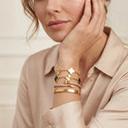 Woman wearing gold bracelets on a neutral background