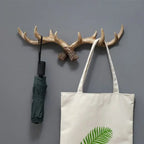 Wooden antler wall hook with a green umbrella and a white tote bag with a leaf design on a gray wall.