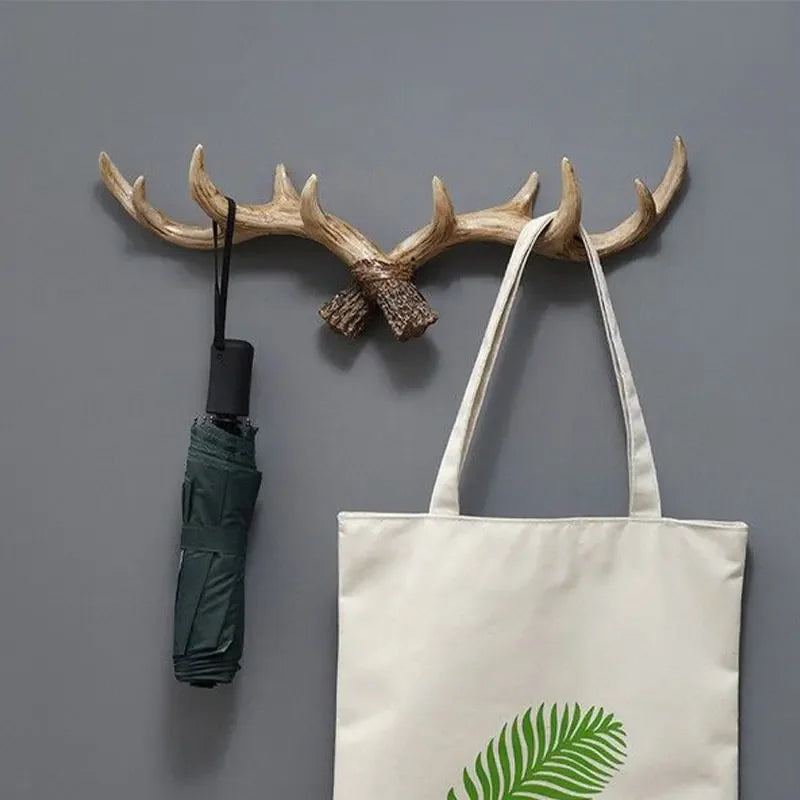 Wooden antler wall hook with a green umbrella and a white tote bag with a leaf design on a gray wall.