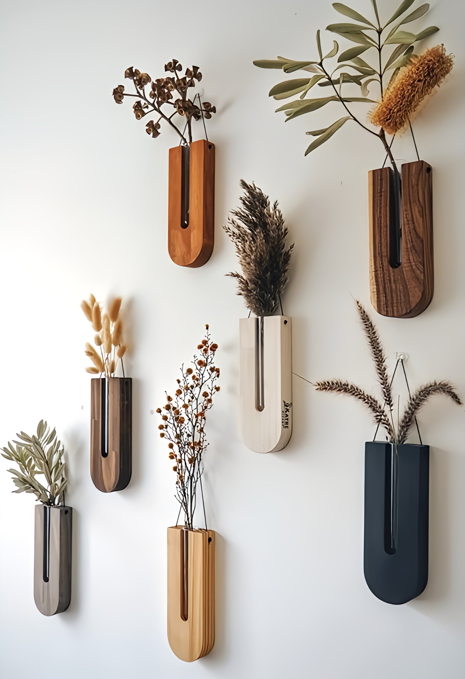 Set of wall-mounted planters with dried plants on a white wall