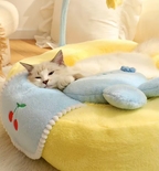 Cat lying on a plush, yellow and blue cushion with a cherry design.