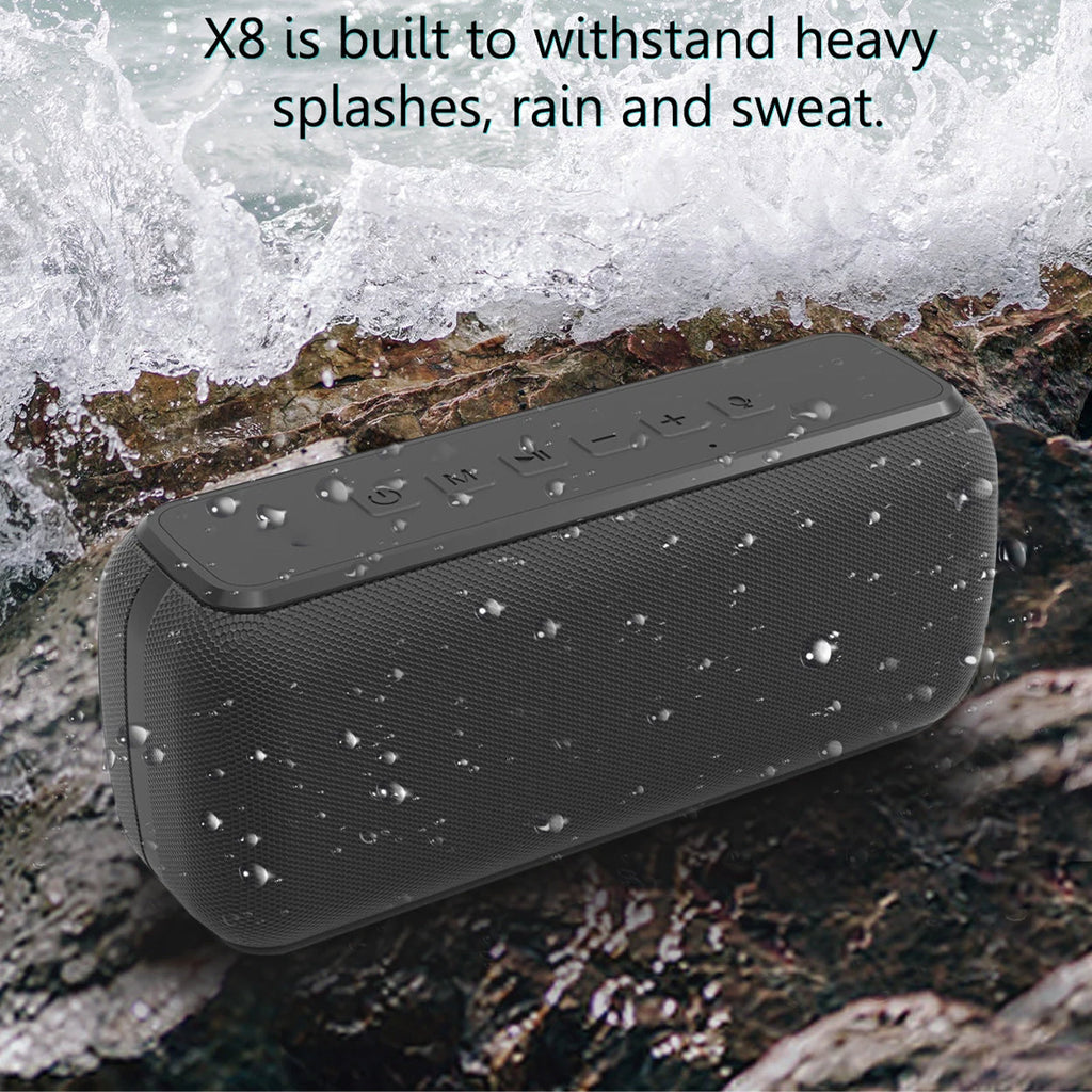 Black portable speaker with water droplets on a rocky surface with water splashing.