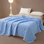 Blue quilted blanket on a bed with white pillows and a lamp in the background.