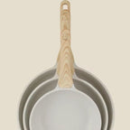 Set of three frying pans with wooden handles on a beige background