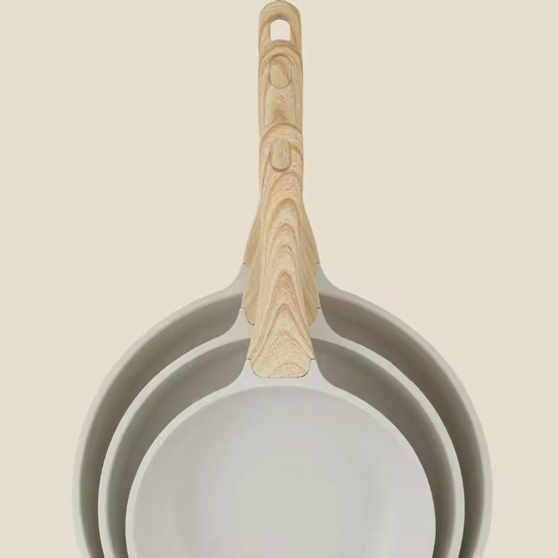 Set of three frying pans with wooden handles on a beige background
