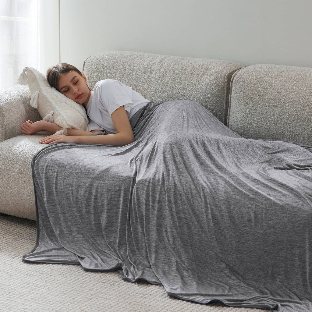 Person lying on a couch under a gray blanket in a cozy living room.