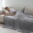 Person lying on a couch under a gray blanket in a cozy living room.
