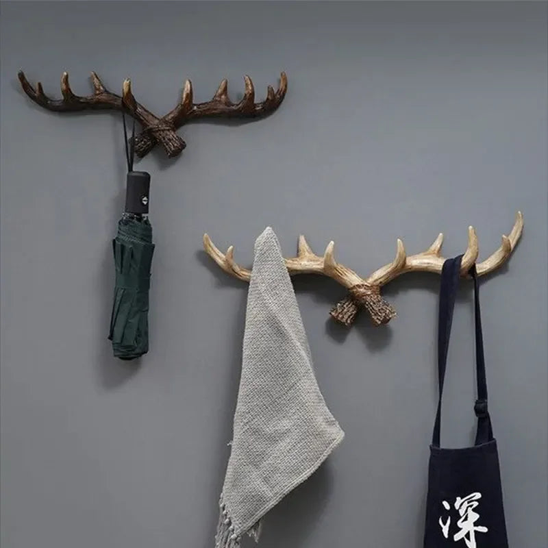Two antler-shaped wall hooks holding an umbrella, towel, and bag on a gray wall.