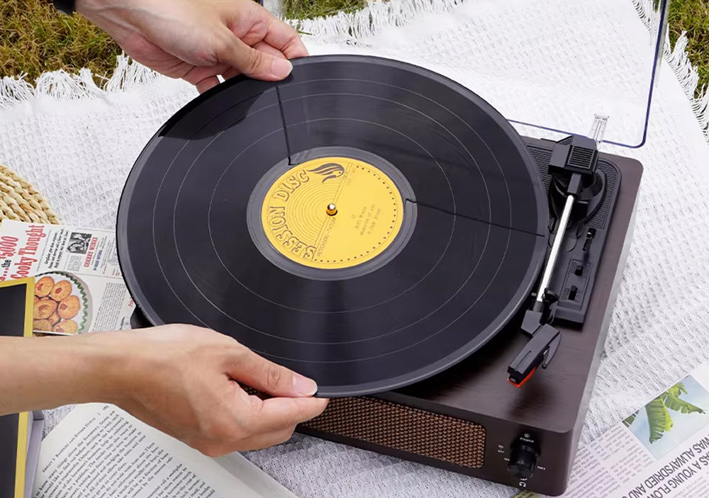 Person placing a vinyl record on a turntable outdoors.