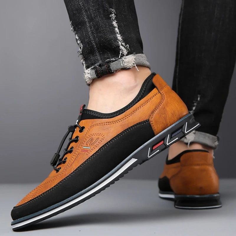 Brown and black leather shoes worn with black jeans on a gray background