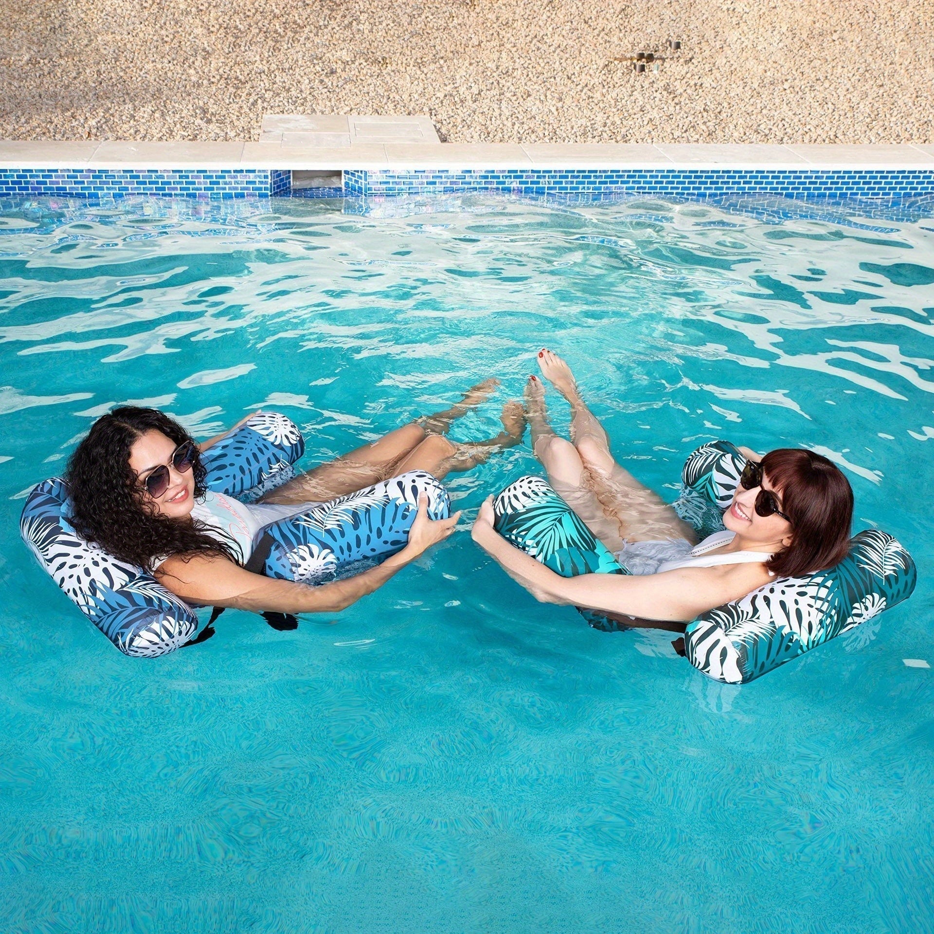 Two people relaxing on inflatable lounge chairs in a pool.