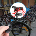 Bicycle lock with a remote control held by a hand, surrounded by bicycles in an outdoor setting.