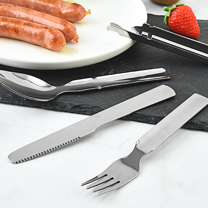 Set of silver cutlery including knife, fork, and spoon on a white surface with sausages and a strawberry in the background.