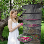 Woman in a white dress standing next to a five-tiered black mesh plant dryer outdoors.