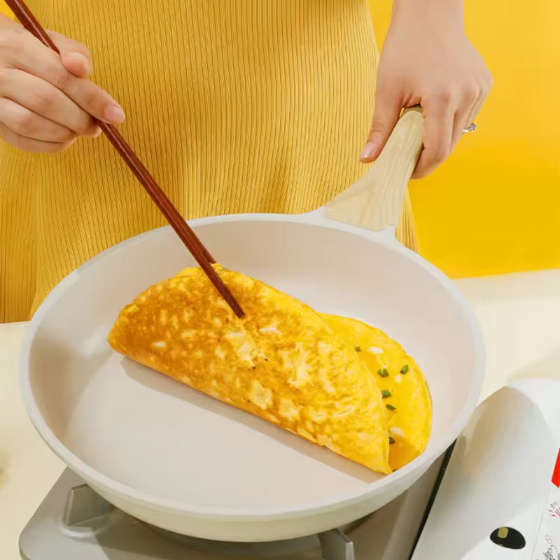 Person using chopsticks to fold an omelette in a white pan with a yellow background