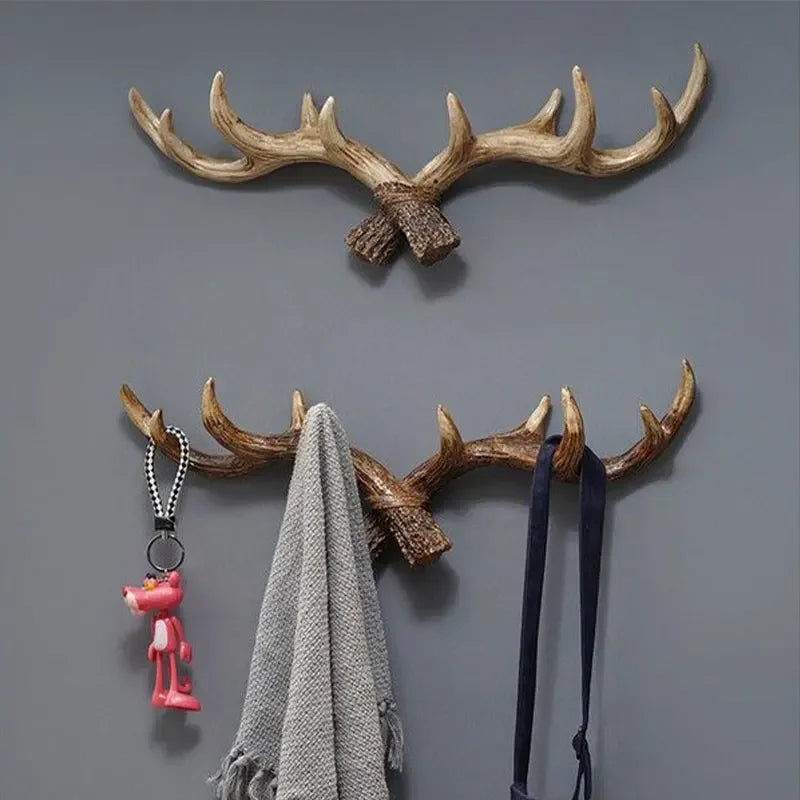 Wall-mounted antler-shaped hooks with a pink keychain, gray scarf, and black belt on a gray background.