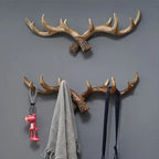 Wall-mounted antler-shaped hooks with a pink keychain, gray scarf, and black belt on a gray background.