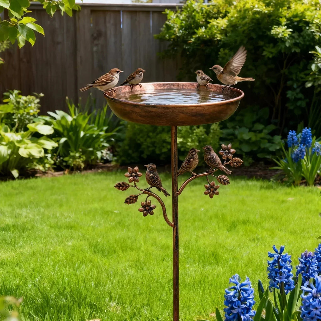 Copper bird bath with birds in a garden setting