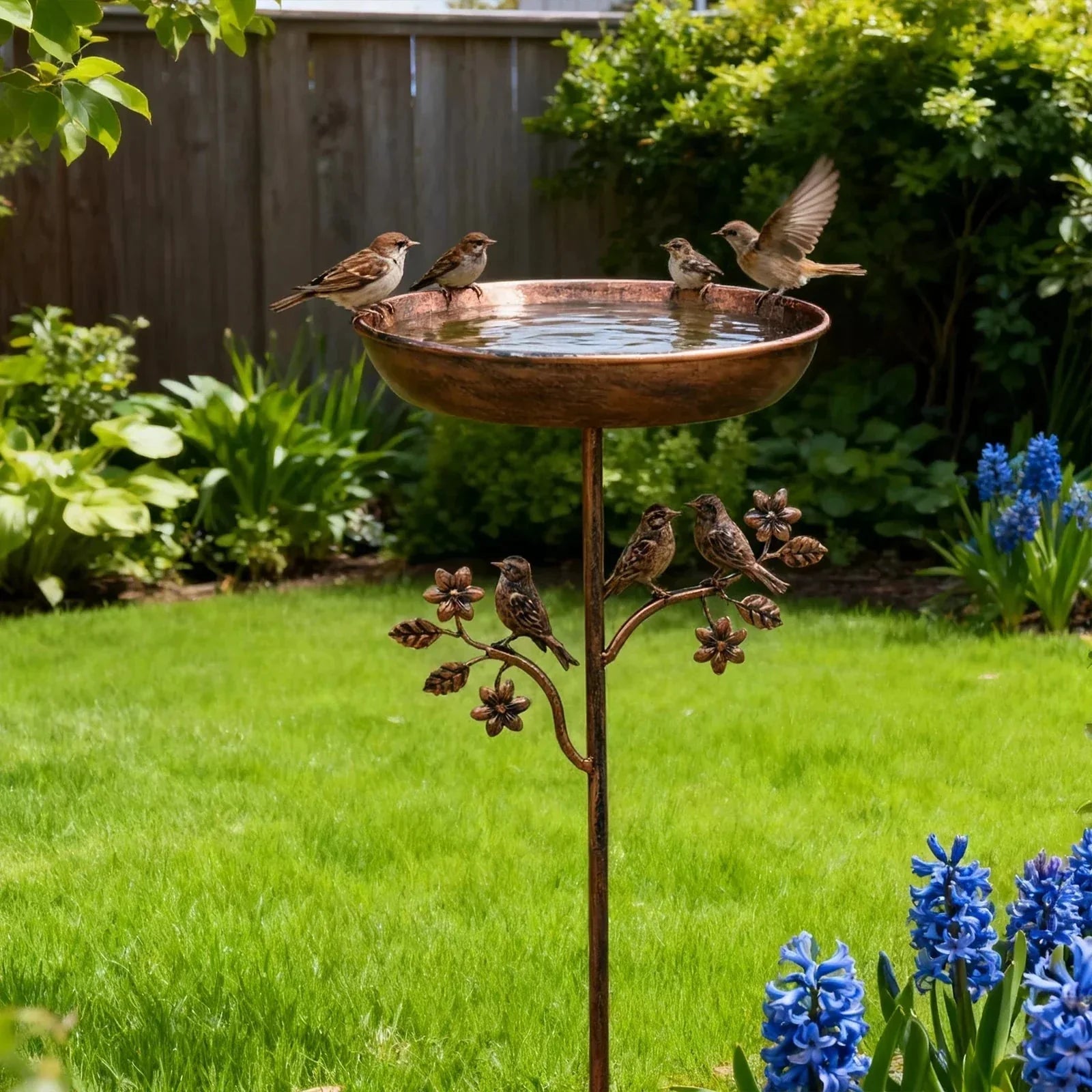Copper bird bath with birds in a garden setting