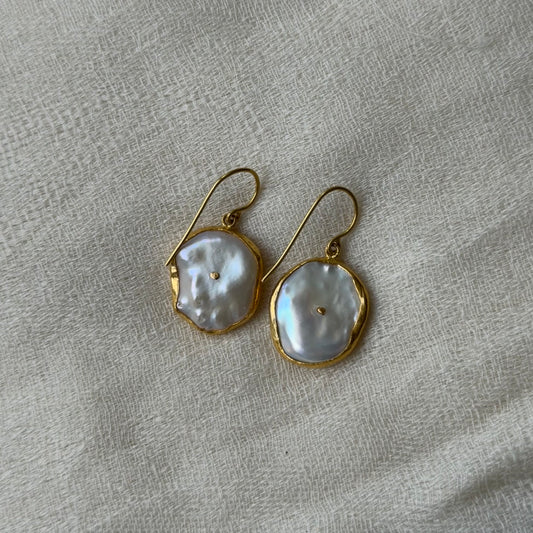 Pair of pearl earrings with 22ct gold frames on a textured gray background