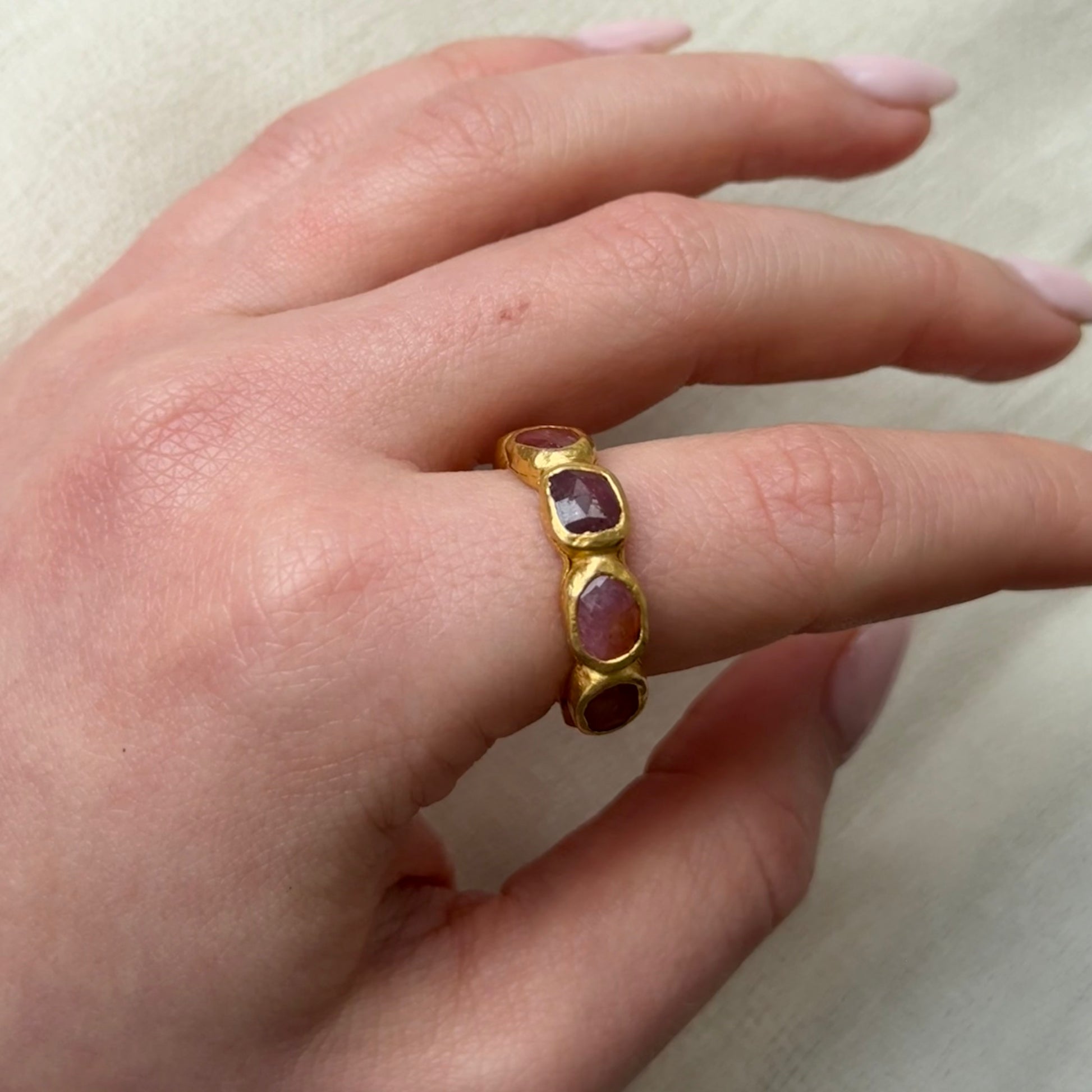 22ct Gold ring with Tourmaline Pink gemstones on a person's finger against a neutral background
