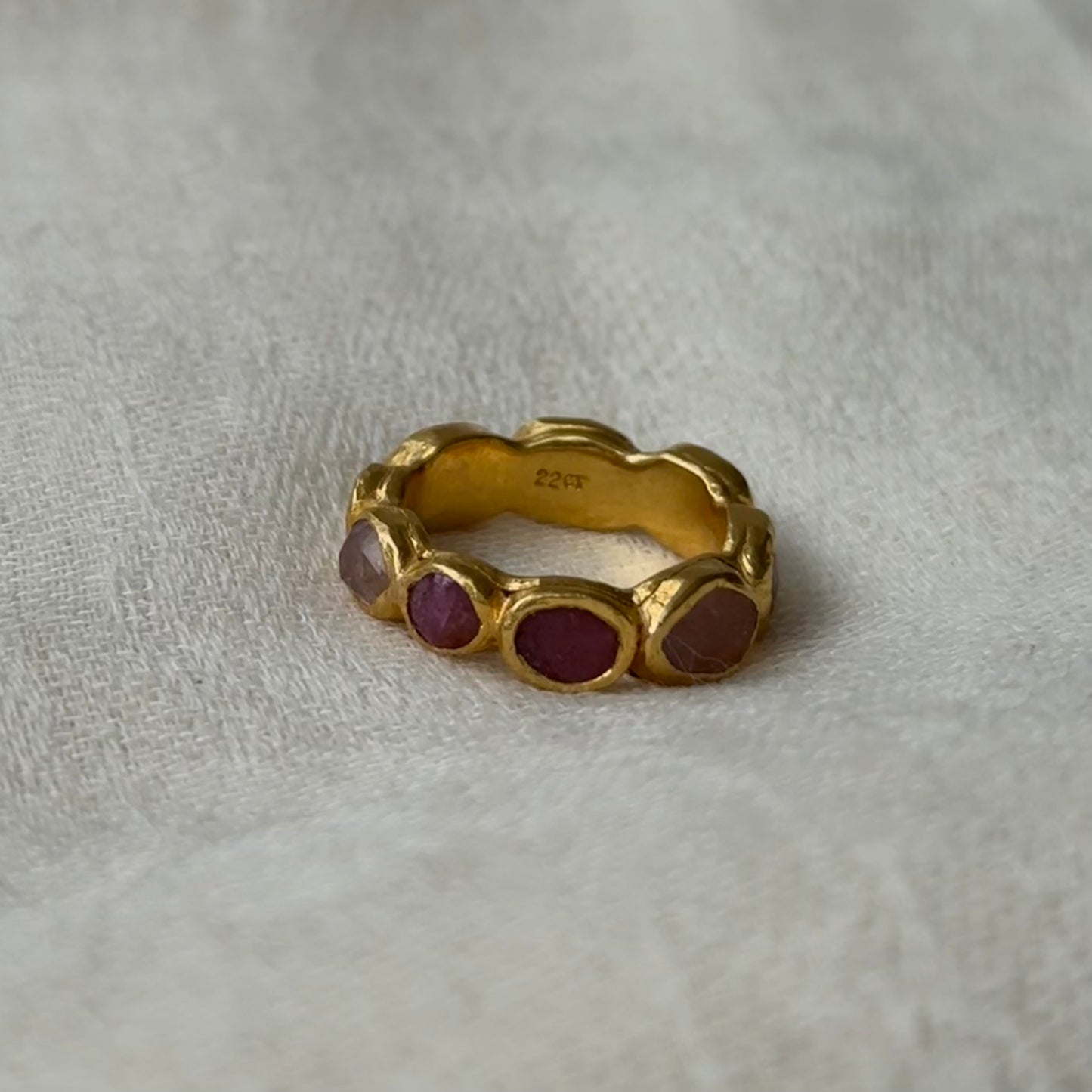 22ct Gold ring with embedded pink tourmaline gems on a light gray fabric background
