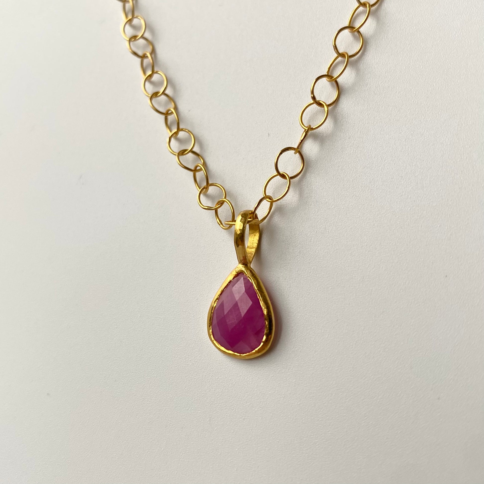 Gold necklace with a teardrop-shaped pink Tourmaline pendant on a light gray background. Designer Ram Rijal
