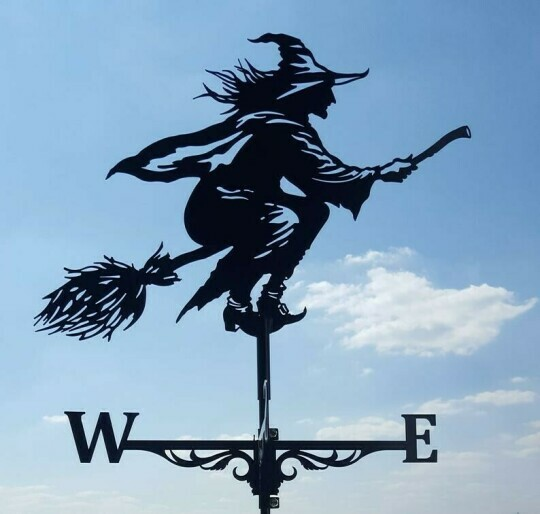 Decorative weather vane shaped like a witch on a broom against a blue sky.