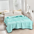 Light blue quilt on a bed in a bright bedroom with white walls and a window.