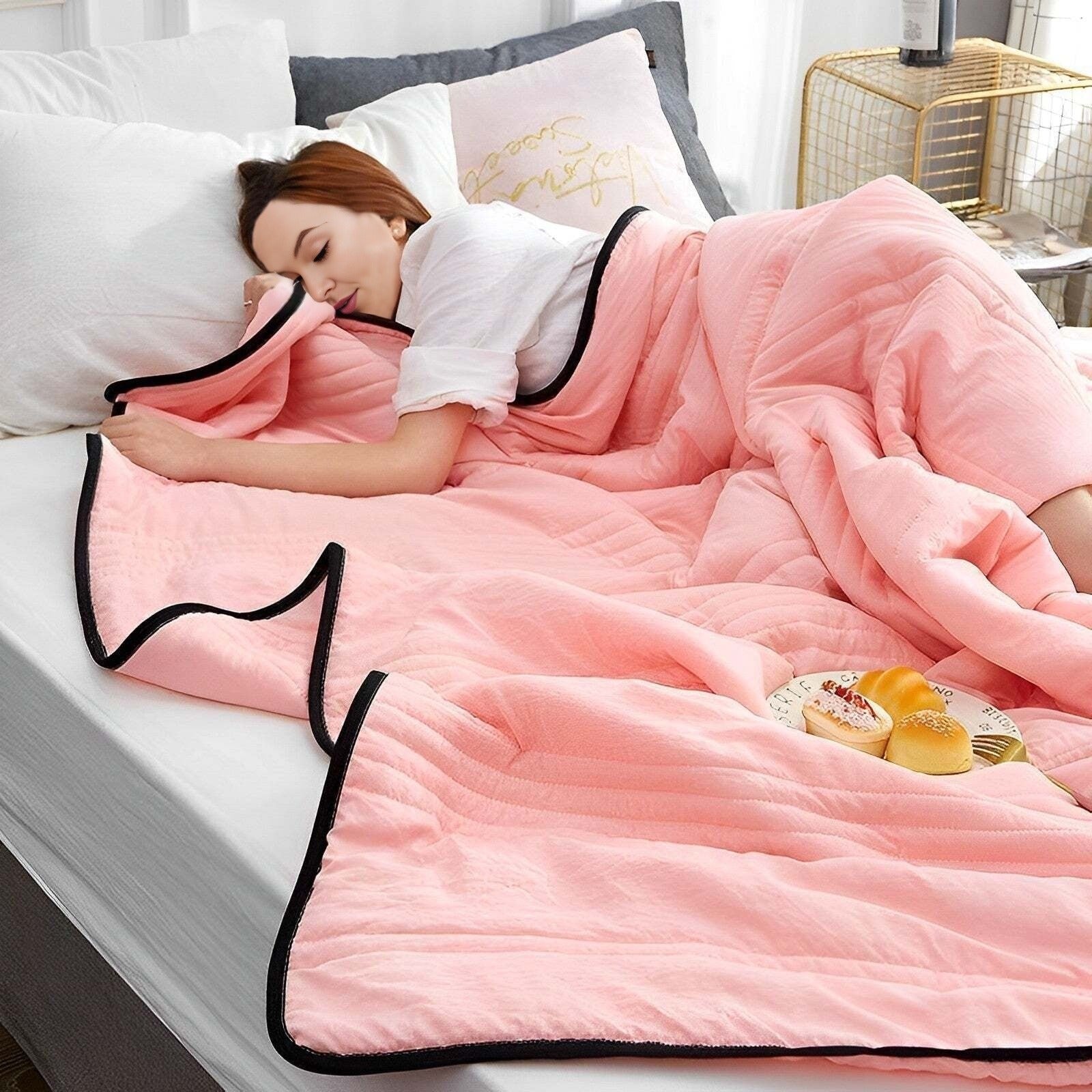 Person lying in bed under a pink comforter with a plate of snacks on a nightstand.