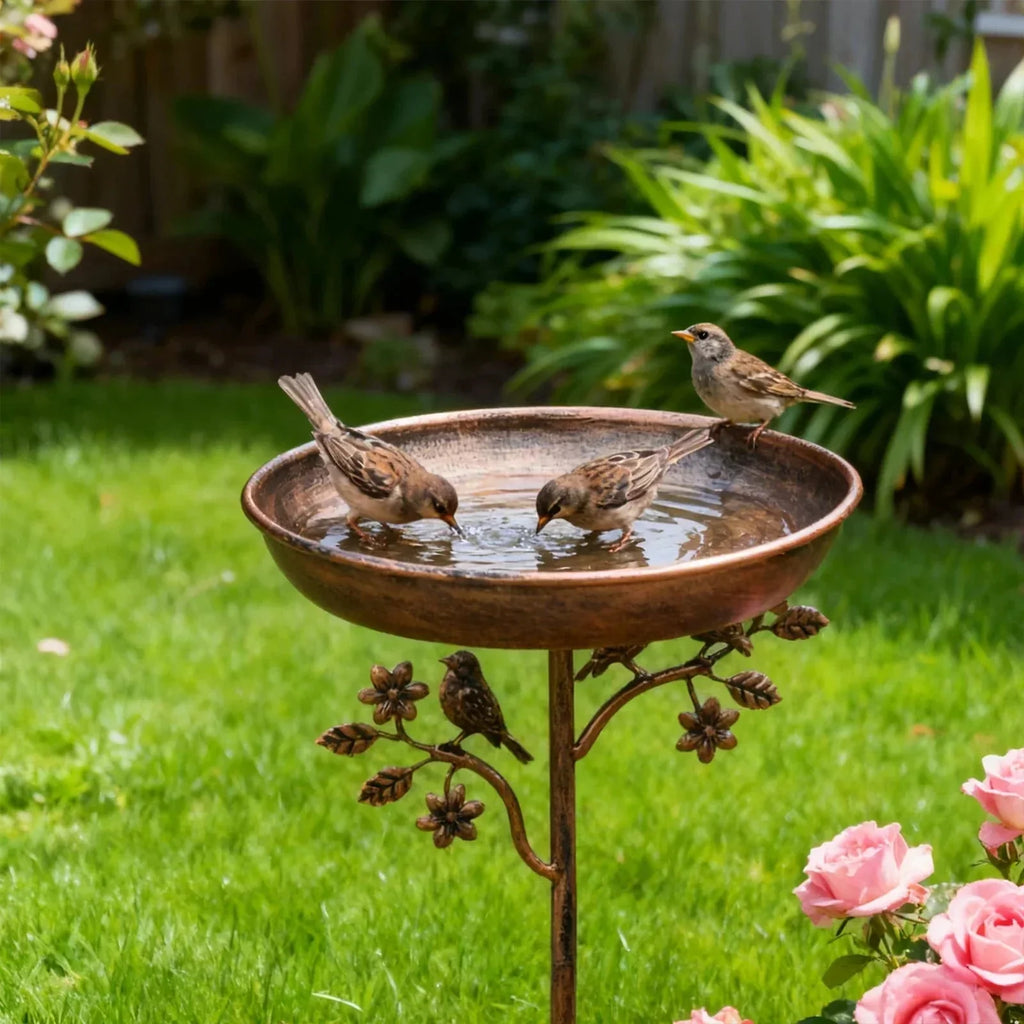 Copper bird bath with birds drinking water in a garden setting