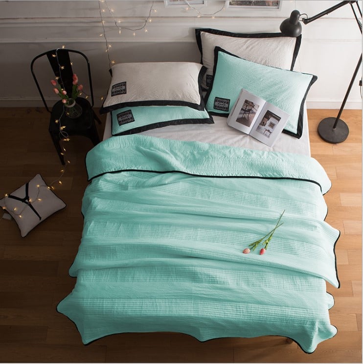 Teal bedspread with black piping on a bed in a bedroom setting.