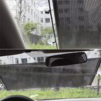 Car sunshade covering a car window with a view of buildings and trees outside.