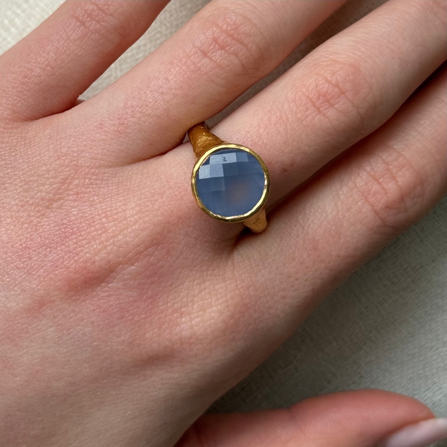 22ct Gold ring with a blue stone on a person's finger against a neutral background