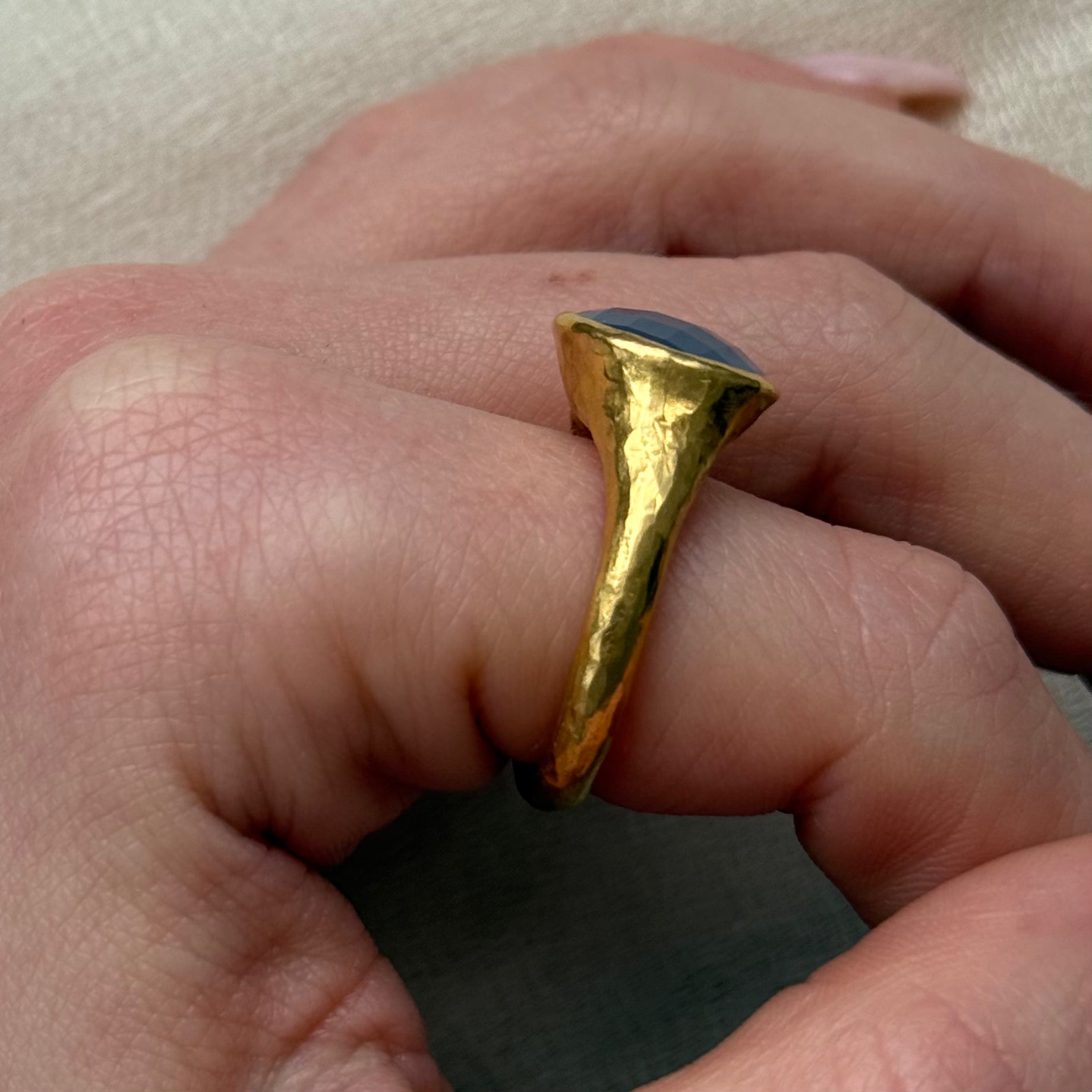 22ct Gold ring with a blue stone on a finger against a neutral background