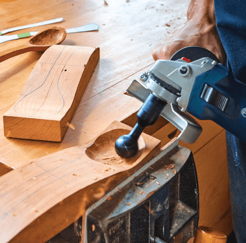 Person using a power tool on a wooden surface with tools and wood pieces.