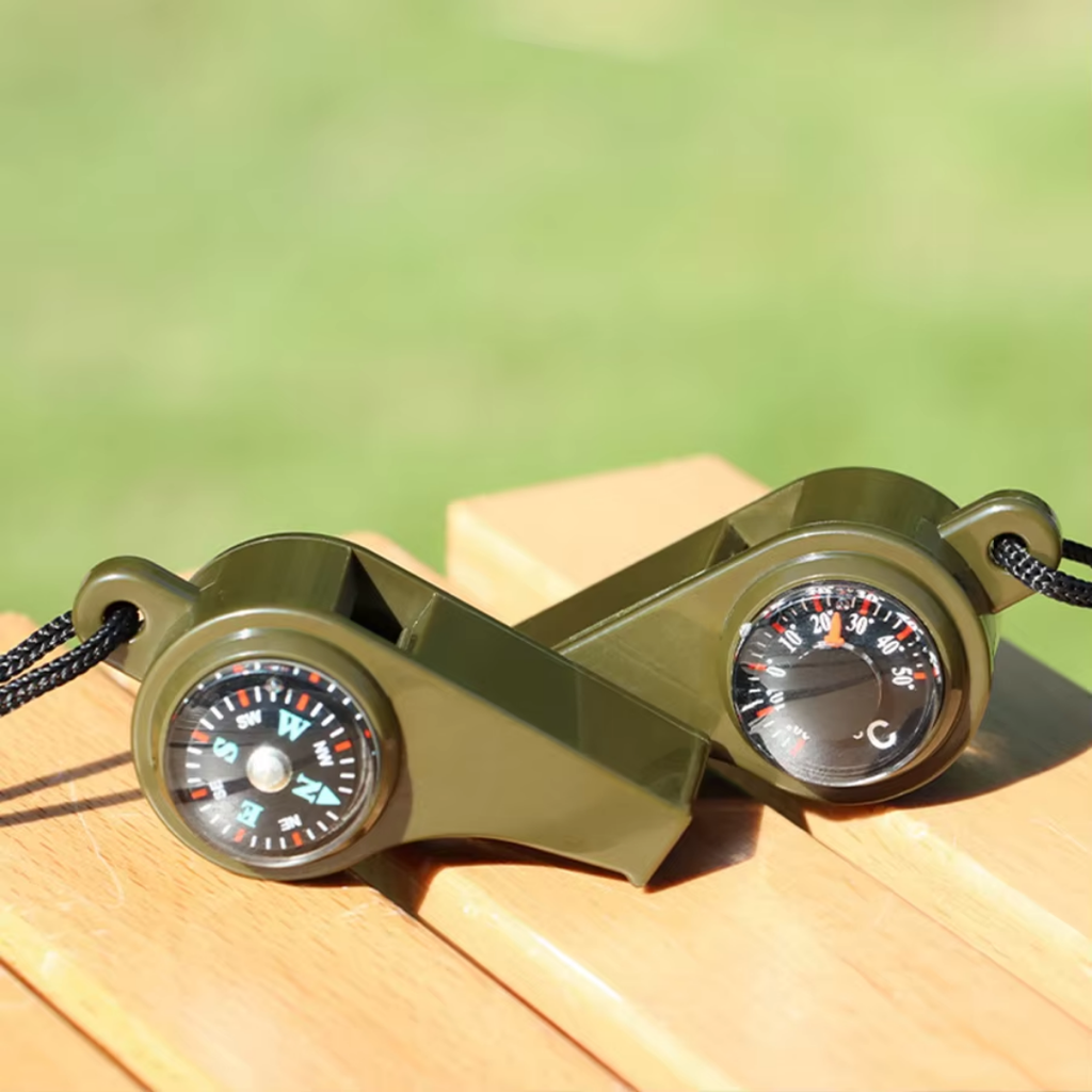 Green binoculars with compass and thermometer on a wooden surface with a blurred green background