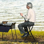 Person sitting on a portable chair by a lake, using a smartphone.