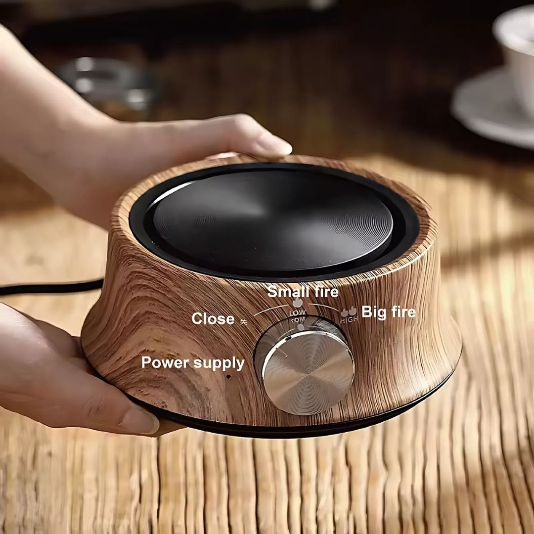 Wooden electric stove with control knob held by a hand on a wooden surface.