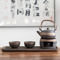 Ceramic teapot and cups on a tray with a blurred calligraphy background
