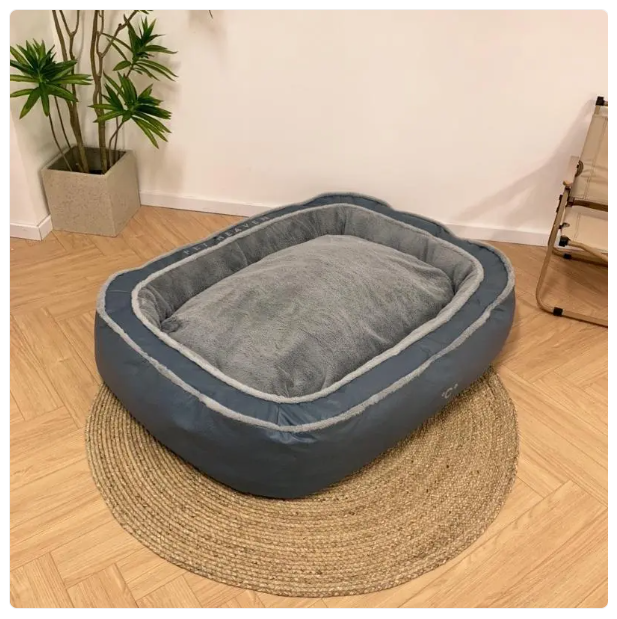 Gray pet bed on a wooden floor with a plant in the background