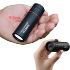 Black monocular held in a hand with close-up detail on a white background